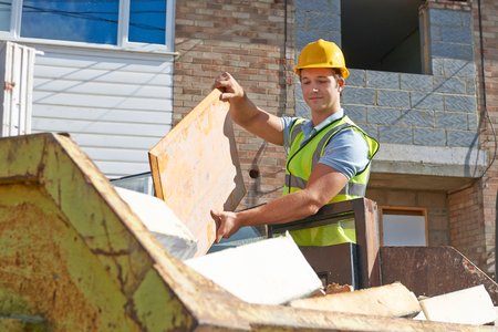 Construction worker placing wood debris into a dumpster